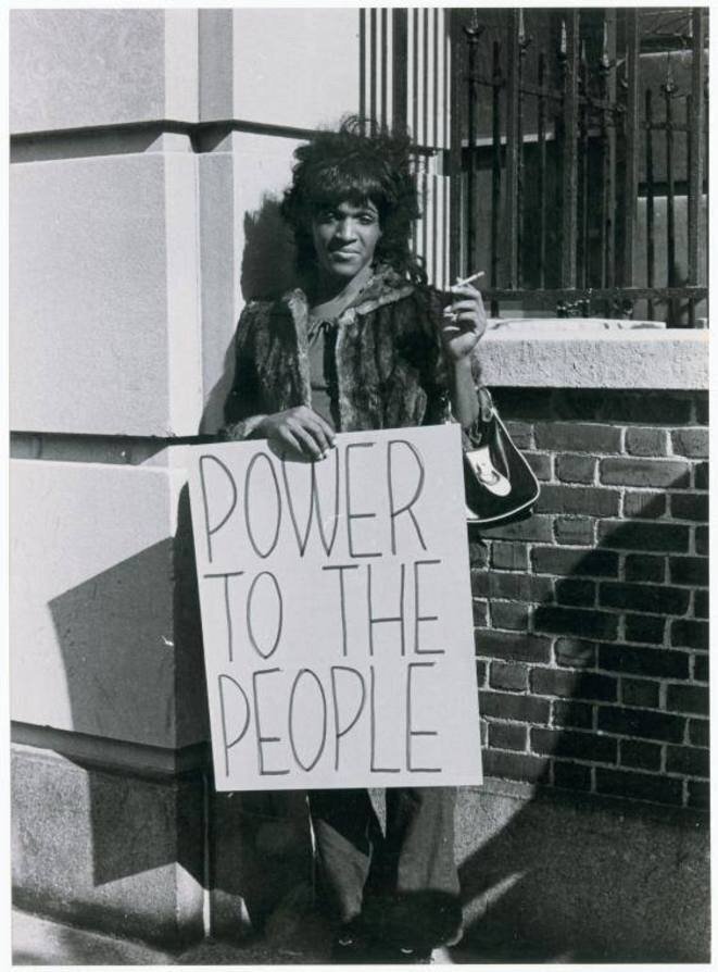 johnson smokes a cigarette outside while holding a sign that says power to the people
