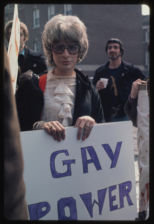 a color photo of rivera holding a sign that says gay power